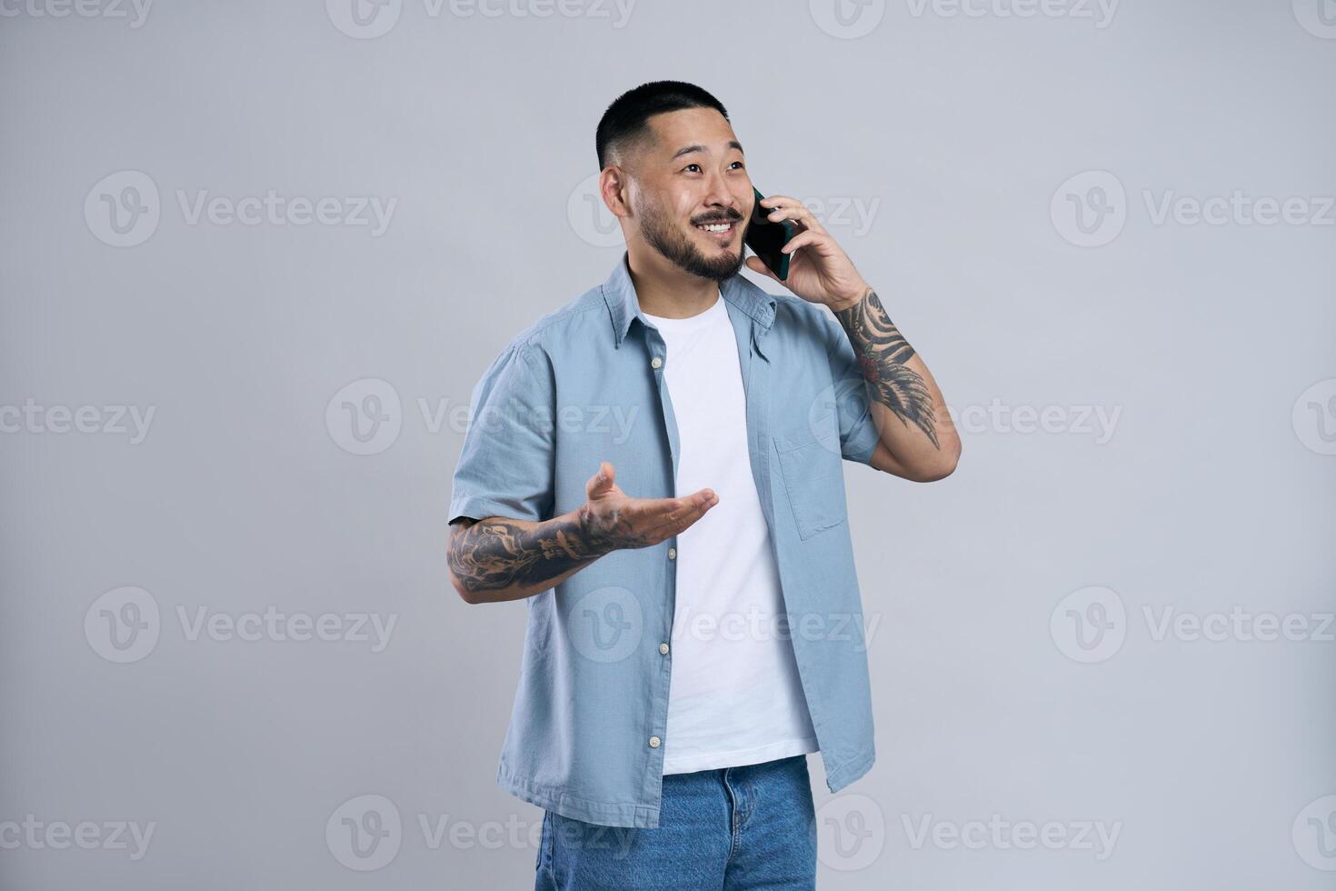 Young asian man with tattoos is talking on the phone and gesturing with hand photo
