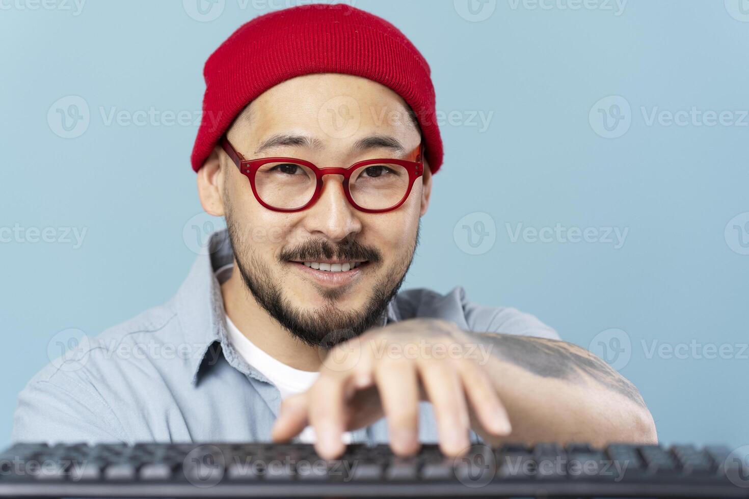 Asian man with red glasses and beanie typing on keyboard photo