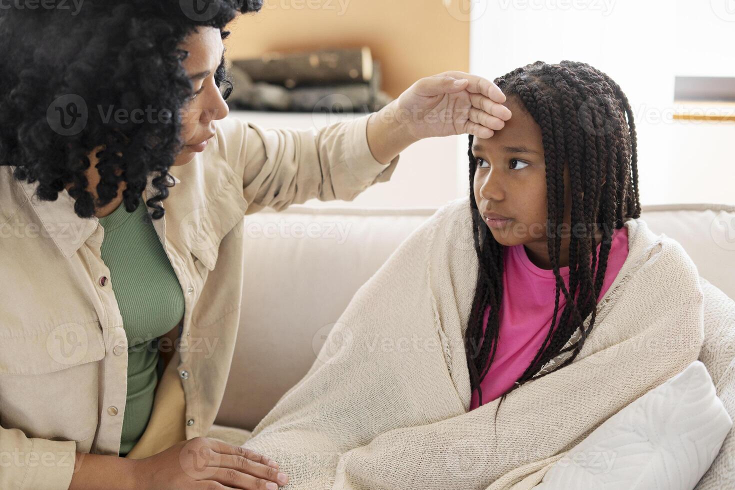 Mother checking daughter's forehead temperature on sofa photo