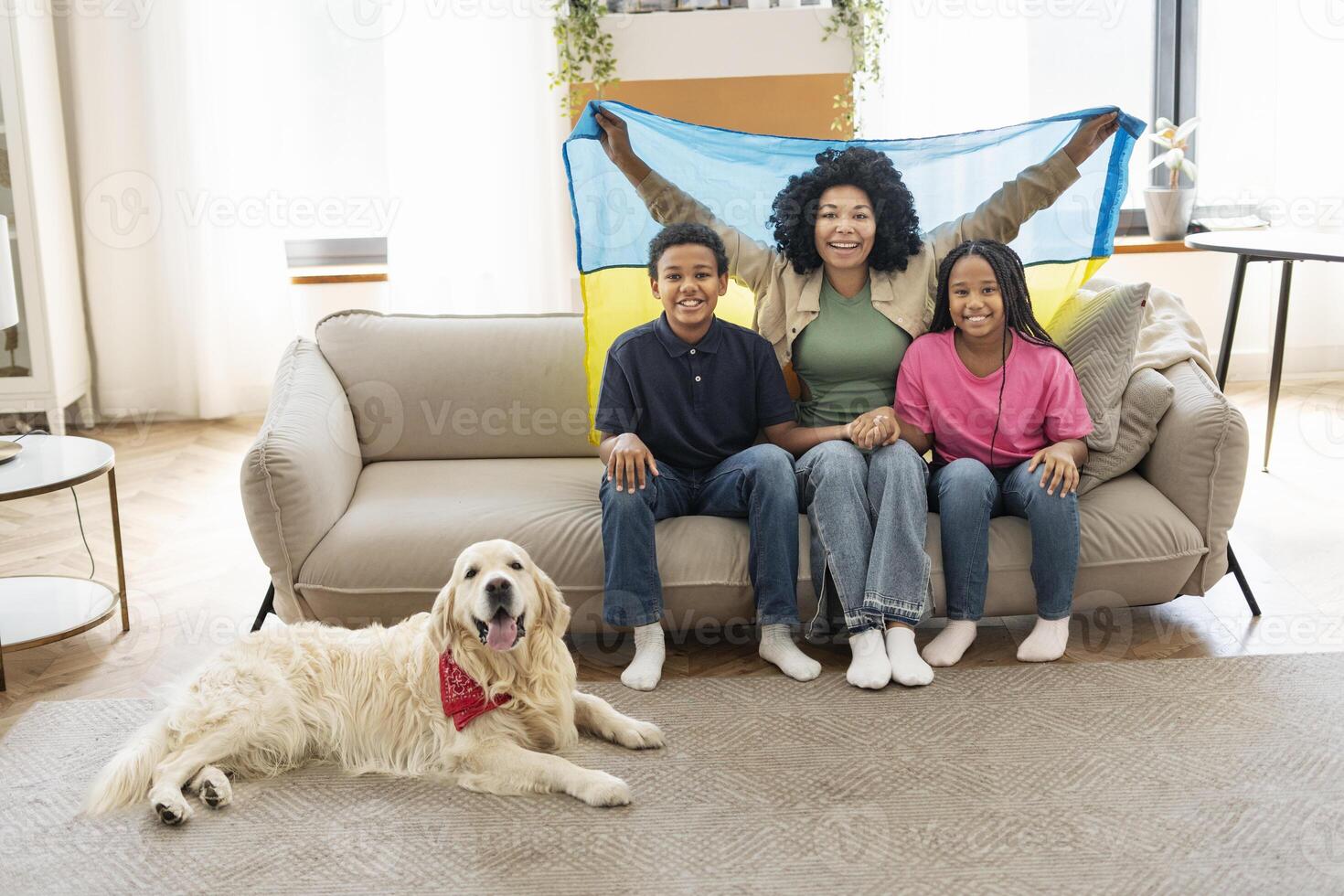 Happy family holding ukrainian flag sitting on sofa with dog at home photo