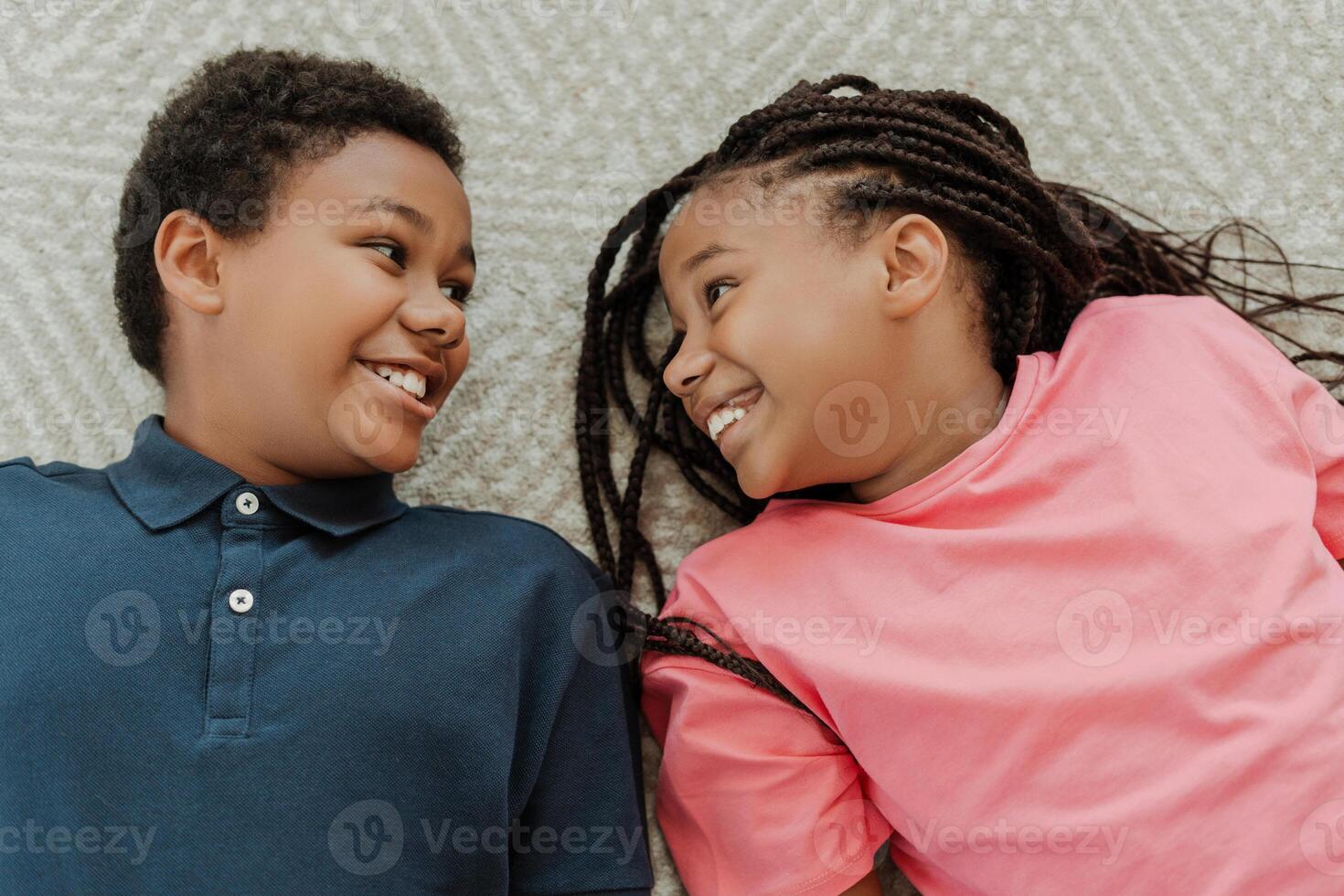 Two happy children lying down on carpet smiling at each other photo