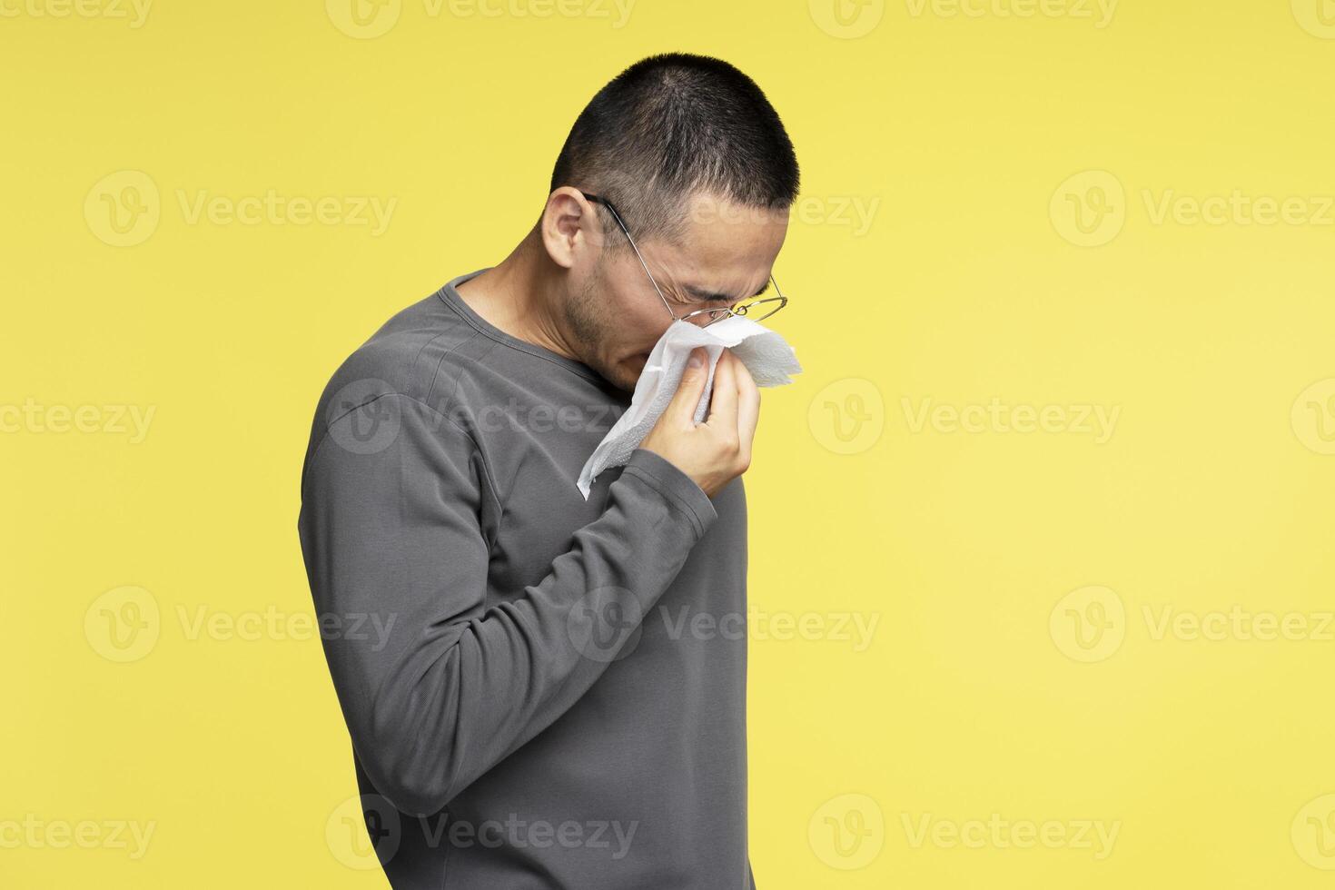 Sick young man blowing his nose with a tissue on yellow background photo