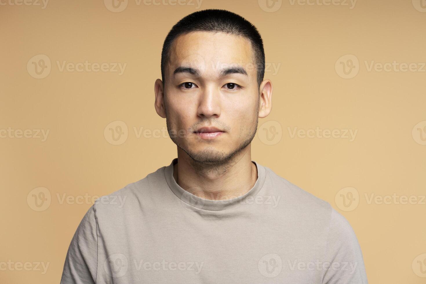 Serious young man with short hair posing on beige background photo