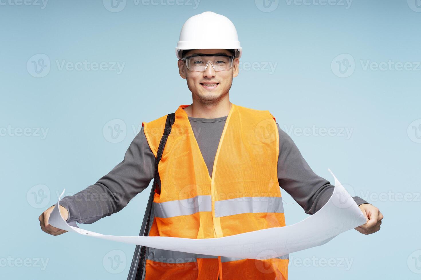 Smiling asian construction worker holding blueprints on blue background photo