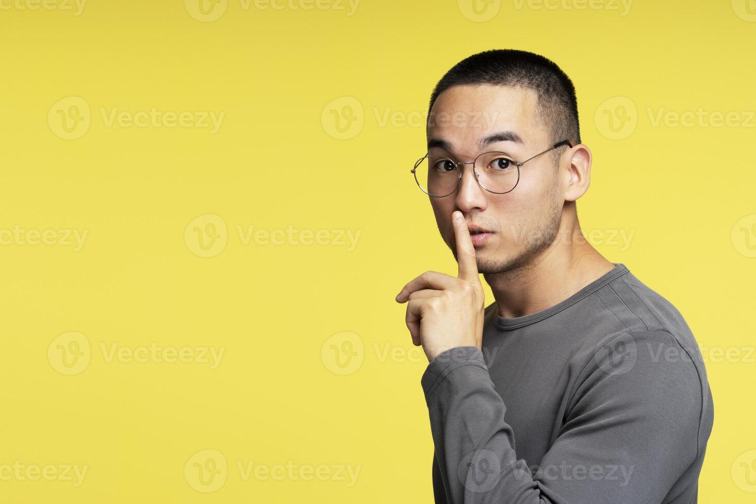 Young man with glasses making silence gesture on yellow background photo