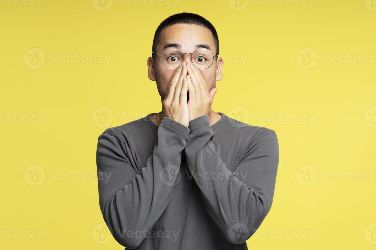 Shocked young man covering his mouth with hands on yellow background photo
