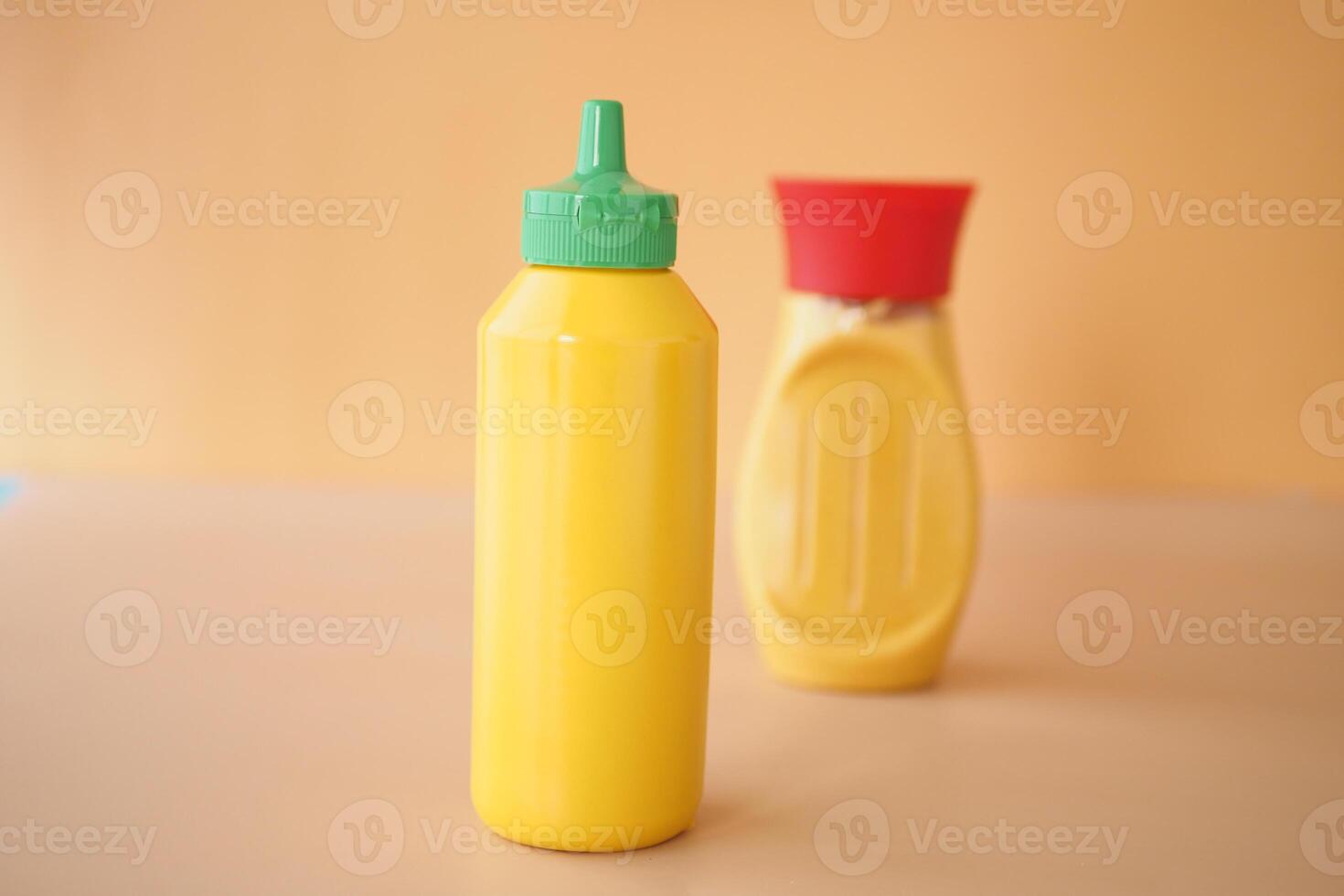 On a table, two vibrant bottles of mustard are displayed, set against a colorful background photo