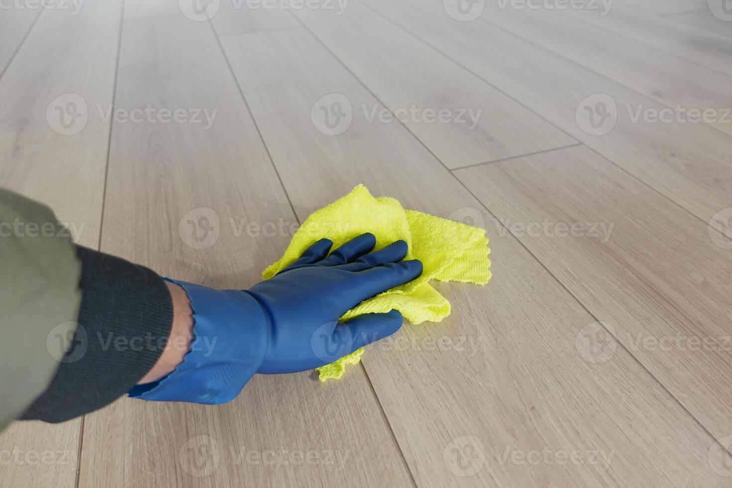 A person is diligently cleaning the floor using a bright yellow cloth and wearing blue gloves photo