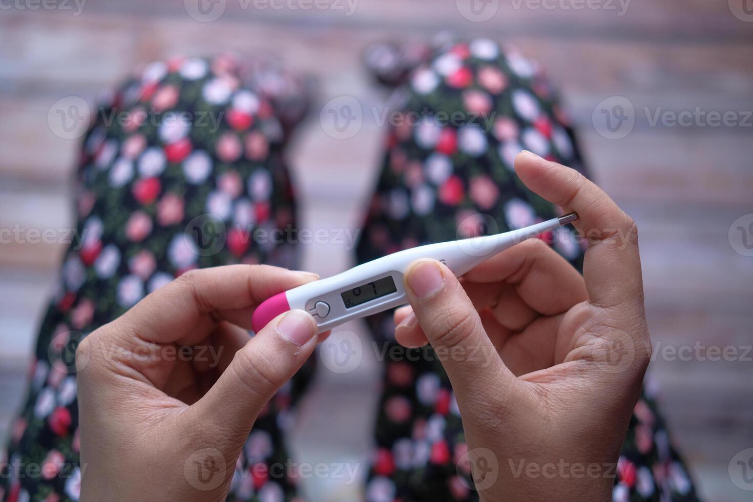 A Woman is Checking a Thermometer for Fever While Relaxing in Cozy Pajamas at Home photo