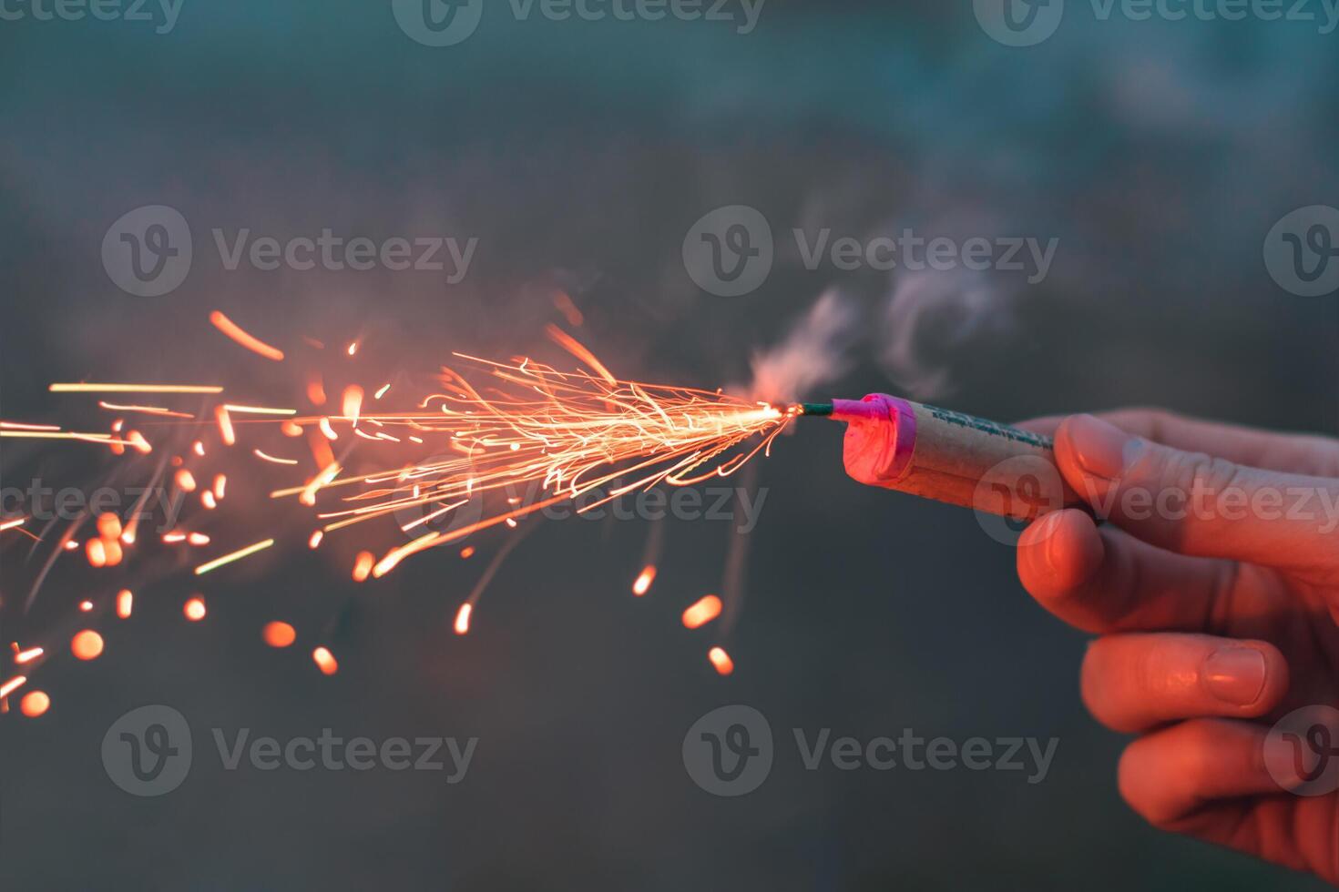 Young Man Lighting Up Firecracker in his Hand Outdoors in Evening. Guy Getting Ready for New Year Fun with Fireworks or Pyrotechnic Products - CloseUp Shot photo