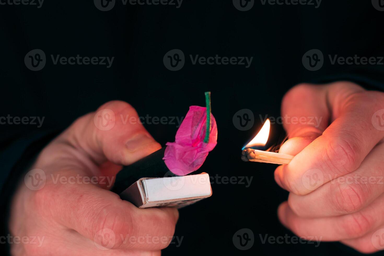 Setting Fire to the Firecracker. Man in Black Clothes Lighting Up the Petard. Pyrotechnics Firing Up with Matches Holding Together with a Matchbox Outdoors photo
