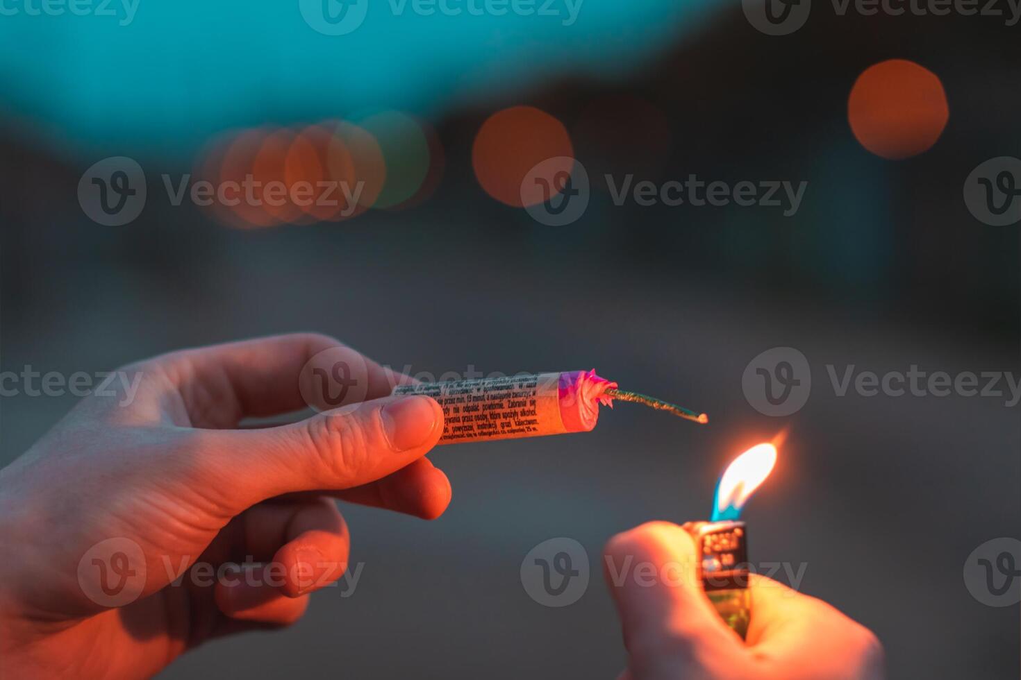 Young Man Lighting Up Firecracker in his Hand Outdoors in Evening. Guy Getting Ready for New Year Fun with Fireworks or Pyrotechnic Products - CloseUp Shot, Rear View photo