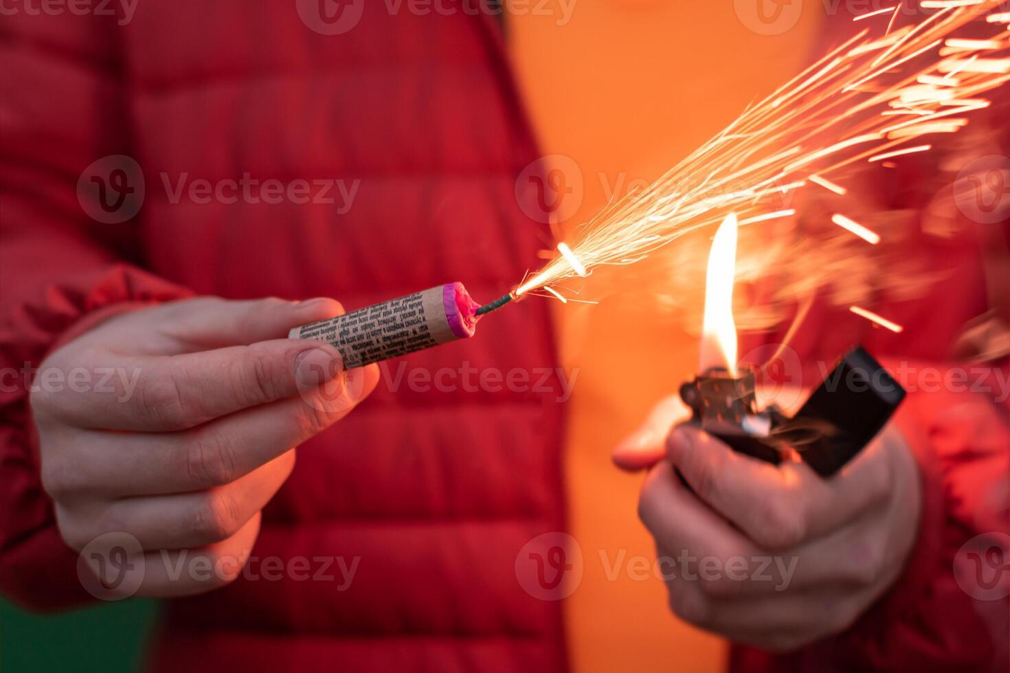 Man in Red Jacked Lighting Up Firecracker in his Hand Using Gasoline Lighter. Guy Getting Ready for New Year Fun with Fireworks or Pyrotechnic Products photo