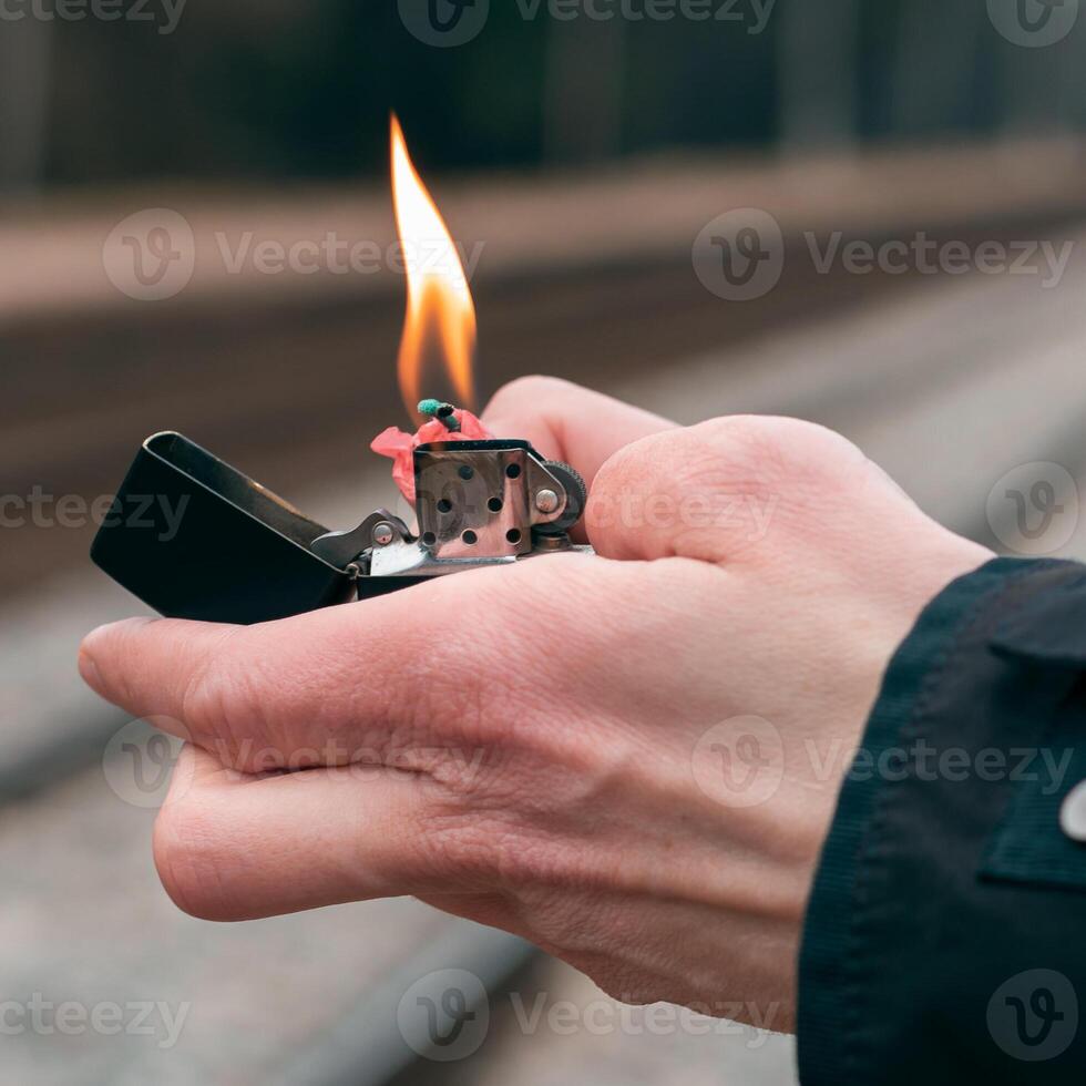 Setting Fire to the Firecracker. Man in Black Clothes Lighting Up the Petard. Firing Up the Pyrotechnics with a Black Gasoline Lighter Outdoors photo
