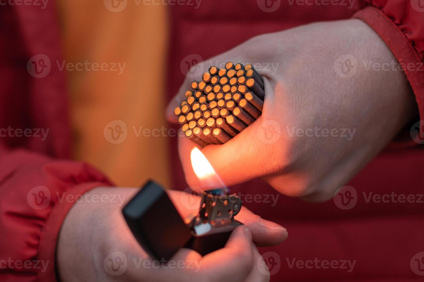 Man in Red Jacked Lighting Up Many Small Black Firecrackers in his Hand Using Gasoline Lighter. Guy Getting Ready for New Year Fun with Fireworks or Pyrotechnic Products photo
