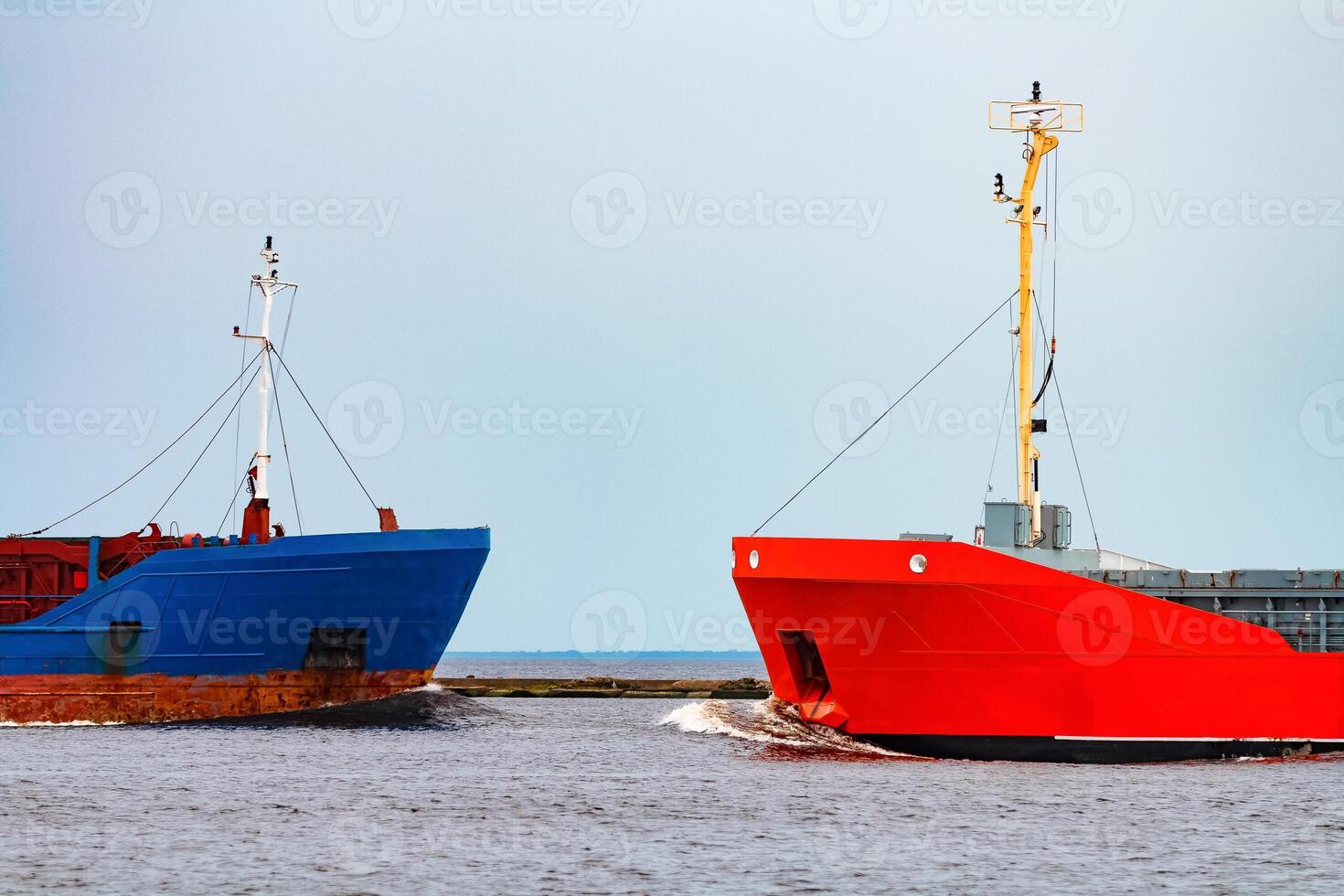 Orange cargo ship sailing past the blue bulk carrier photo