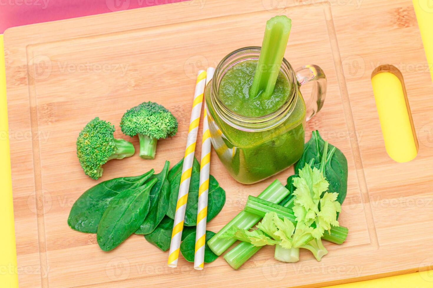 Fresh Green Smoothie of Apple, Celery, and Spinach in Glass Smoothie Jar with Yellow Cocktail Straw on Wooden Cutting Board. Vegan Detox Drink. Vegetarian Culture. Healthy Eating and Fruit Diet photo