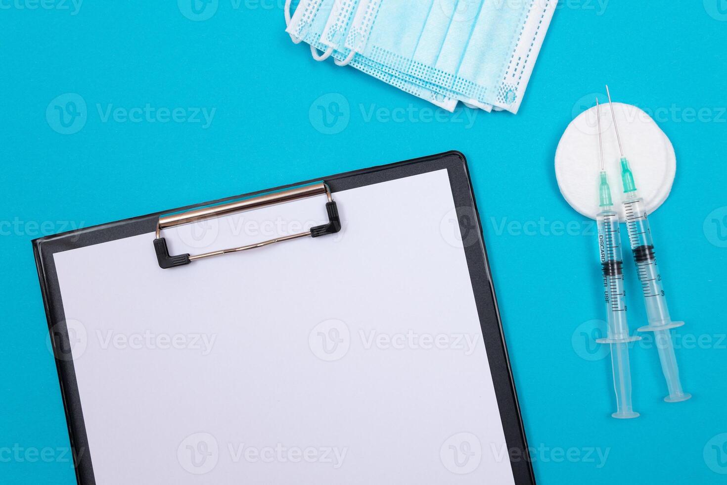 Vaccination, Immunology or Revaccination Concept - Two Medical Syringe Lying on Blue Table in Doctor's Office in a Hospital or Clinic. Black Clipboard with Sheet of Paper - Mock Up with Copy Space photo