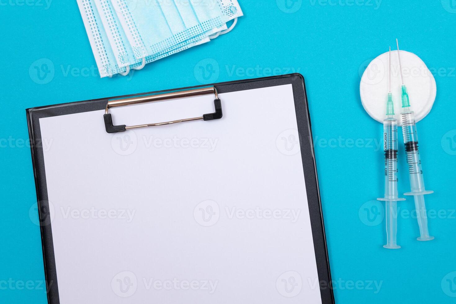 Vaccination, Immunology or Revaccination Concept - Two Medical Syringe Lying on Blue Table in Doctor's Office in a Hospital or Clinic. Black Clipboard with Sheet of Paper - Mock Up with Copy Space photo
