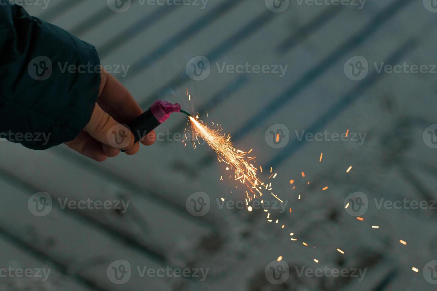 Burning Firecracker with Sparks. Guy Holding a Petard in a Hand. Loud and Dangerous New Year's Entertainment. Hooliganism with Pyrotechnics. Noise of Firecrackers in Public Places photo