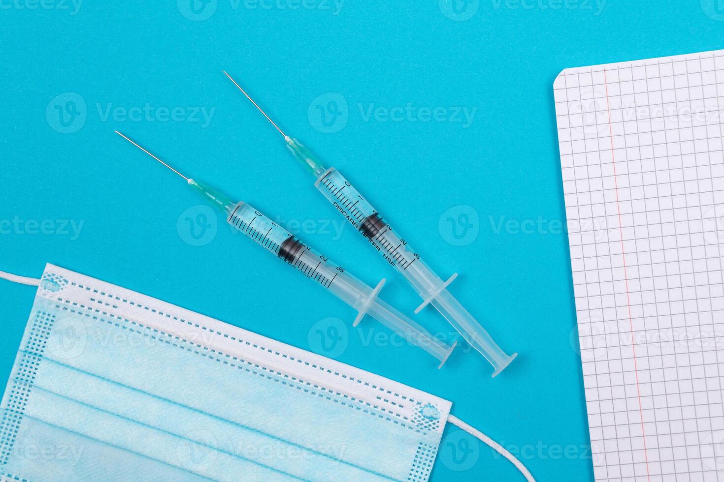 Vaccination, Immunology or Revaccination Concept - Two Medical Syringe Lying on Blue Table in Doctor's Office in a Hospital or Clinic. Opened Blank Notepad - Mock Up with Copy Space photo