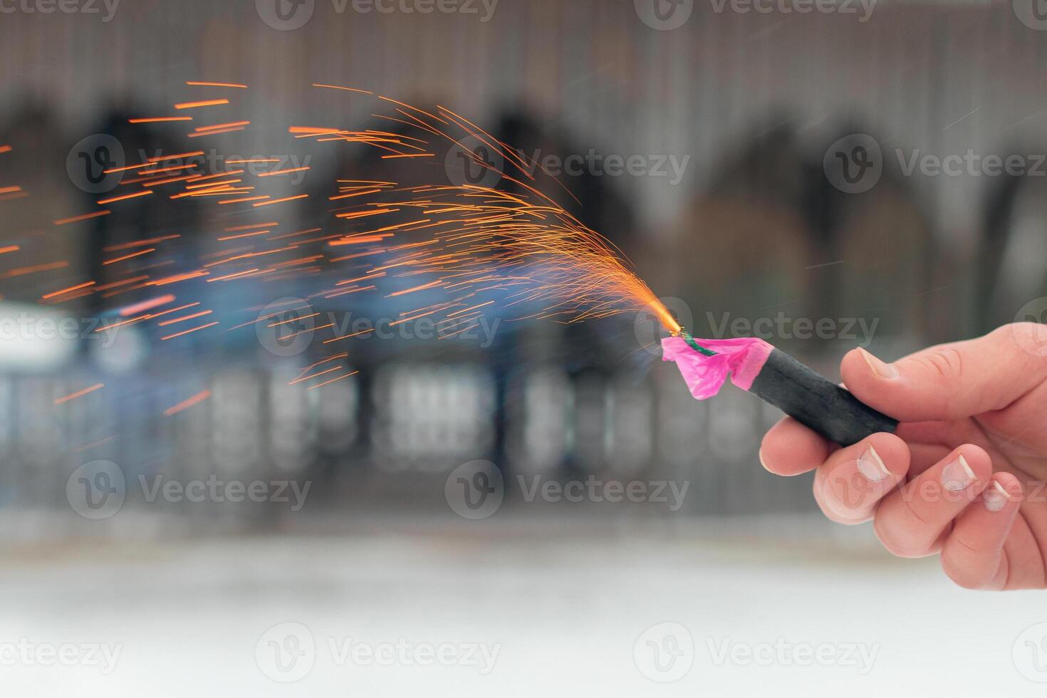 Burning Firecracker in a Hand. Guy Holding a Petard Outdoors in Winter at Daytime. Loud and Dangerous New Year's Entertainment. Hooliganism with Pyrotechnics. Noise of Firecrackers in Public Places photo