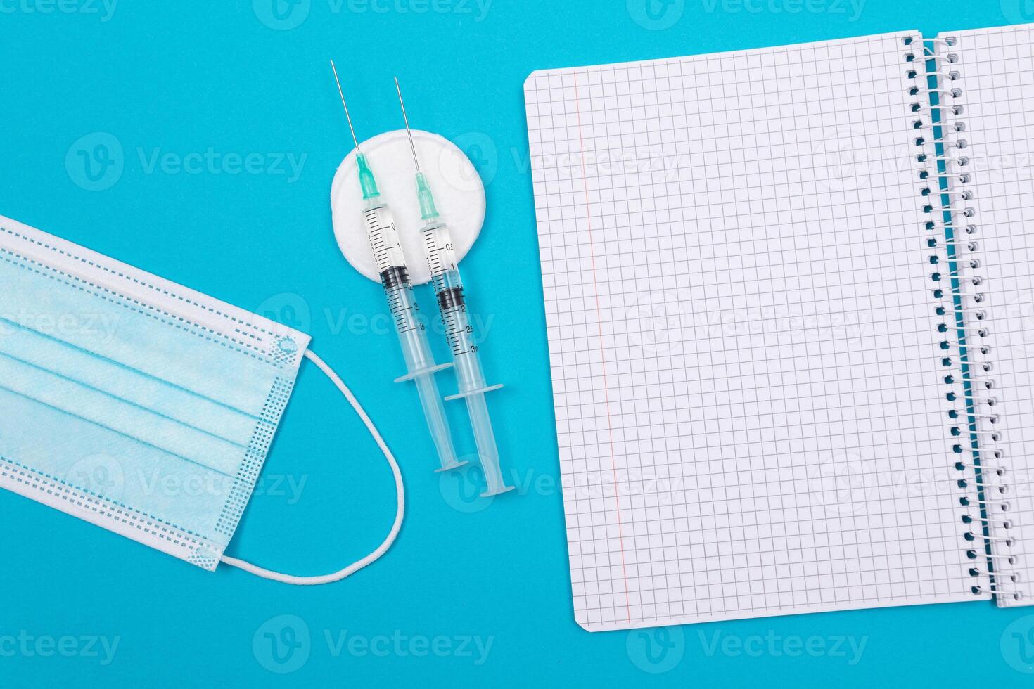 Vaccination, Immunology or Revaccination Concept - Two Medical Syringe Lying on Blue Table in Doctor's Office in a Hospital or Clinic. Opened Blank Notepad - Mock Up with Copy Space photo
