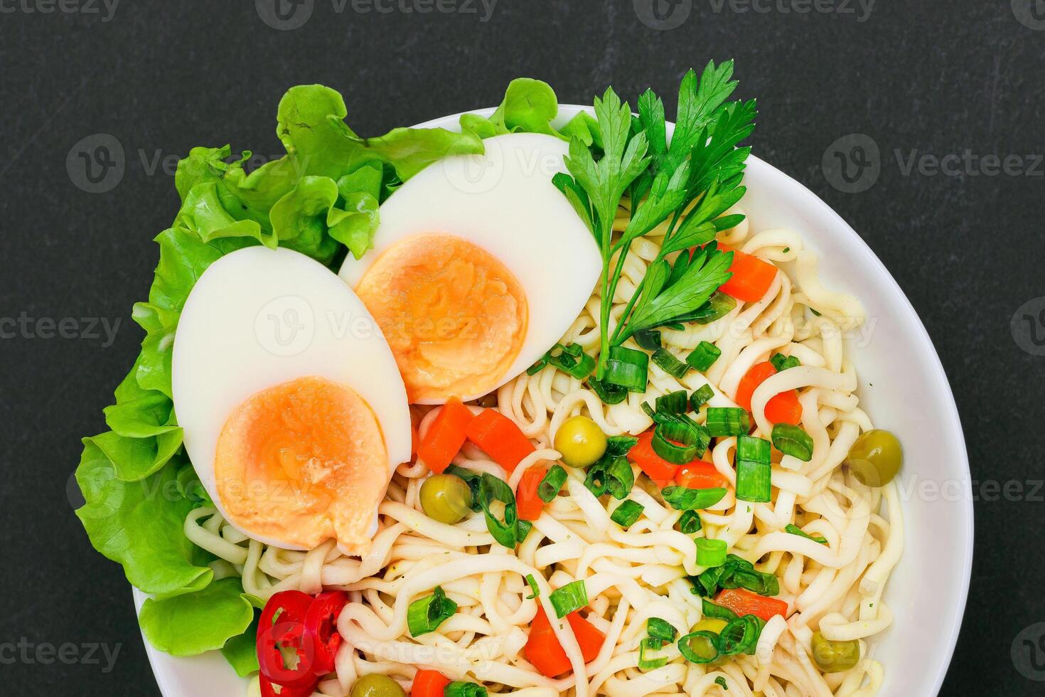 Beautiful Noodle Dish with Green Pea, Carrot, Eggs, Red Hot Pepper and Greens on Black Background. Instant Noodles with Vegetables photo