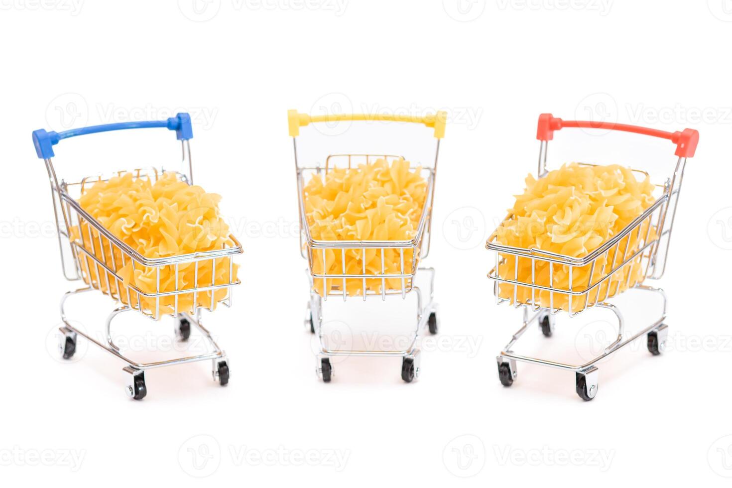 Uncooked Fusilli Pasta in Three Small Shopping Carts Isolated on White Background. A Crisis. Buying Cheap Food. Classic Dry Spiral Macaroni. Italian Culture and Cuisine. Raw Pasta - Isolation photo