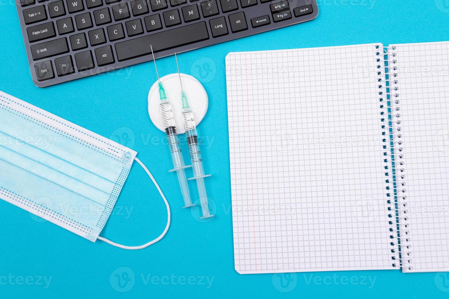 Vaccination, Immunology or Revaccination Concept - Two Medical Syringe Lying on Blue Table in Doctor's Office in a Hospital or Clinic. Opened Blank Notepad - Mock Up with Copy Space photo