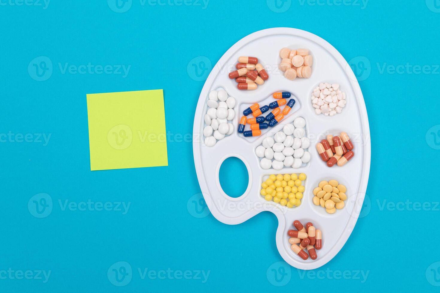 Global Pharmaceutical Industry and Medicinal Products - Different Colored Pills, Tablets and Capsules on White Art Palette with Blank Sticky Note and Copy Space Lying on Blue Background, Flat Lay photo