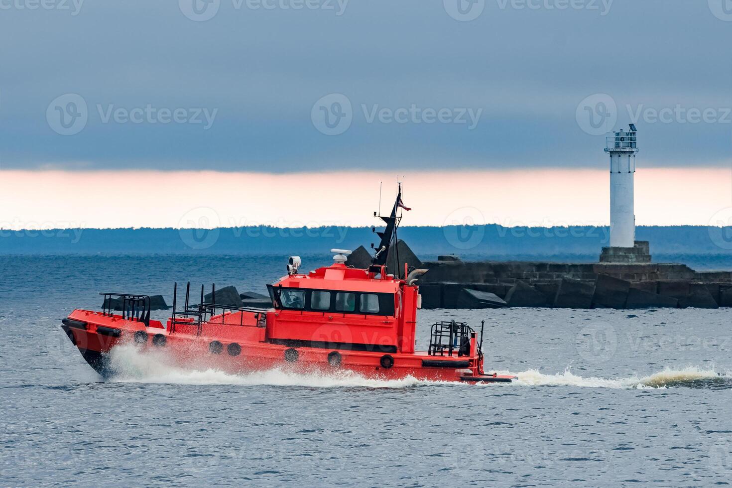Red pilot ship moving at speed past the lighthouse in Riga photo