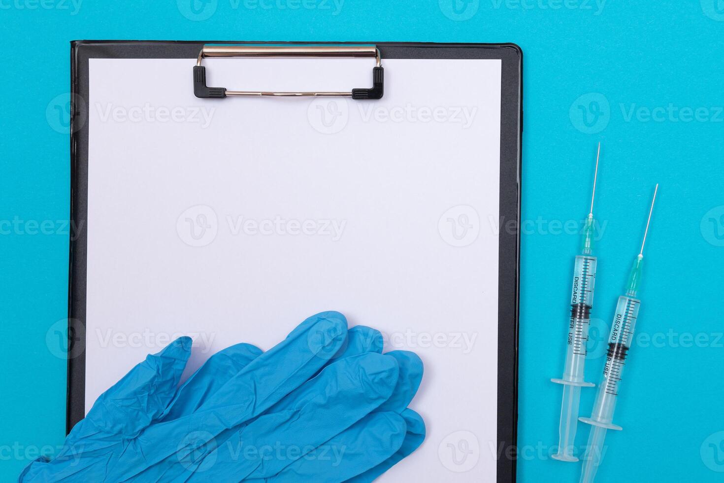 Vaccination, Immunology or Revaccination Concept - Two Medical Syringe Lying on Blue Table in Doctor's Office in a Hospital or Clinic. Black Clipboard with Sheet of Paper - Mock Up with Copy Space photo