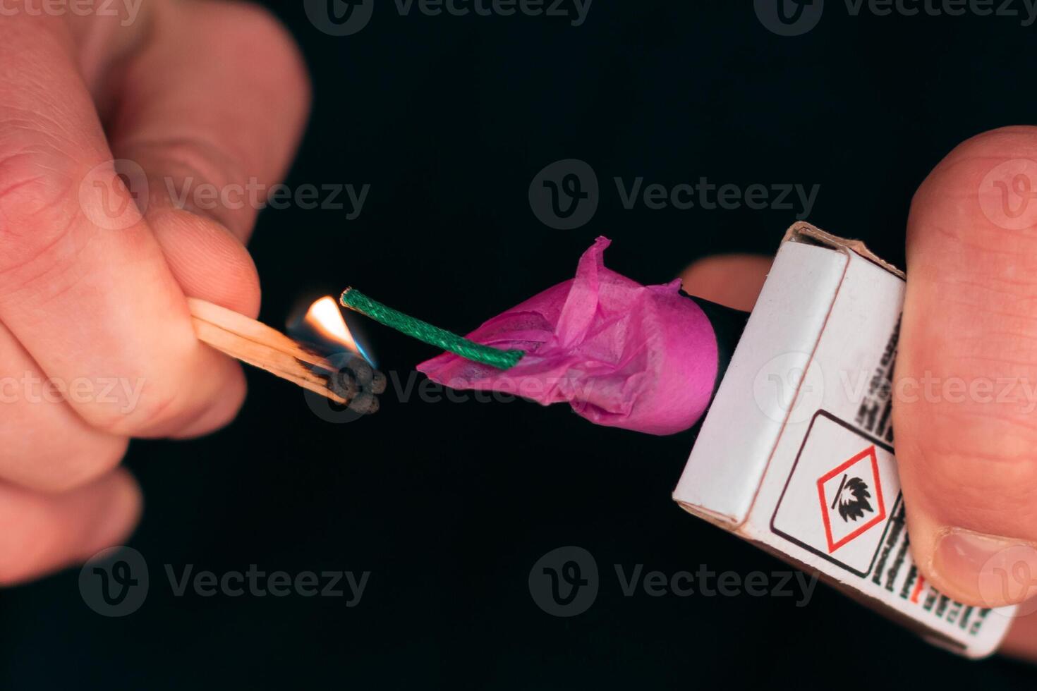Setting Fire to the Firecracker. Man in Black Clothes Lighting Up the Petard. Pyrotechnics Firing Up with Matches Holding Together with a Matchbox Outdoors photo