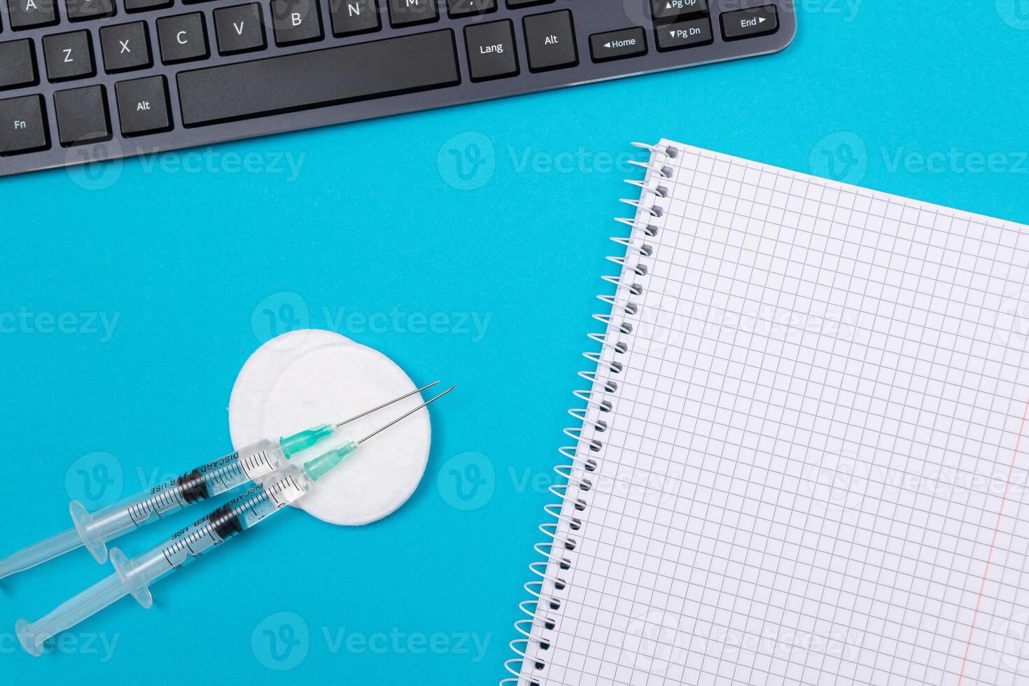 Vaccination, Immunology or Revaccination Concept - Two Medical Syringe Lying on Blue Table in Doctor's Office in a Hospital or Clinic. Opened Blank Notepad - Mock Up with Copy Space photo