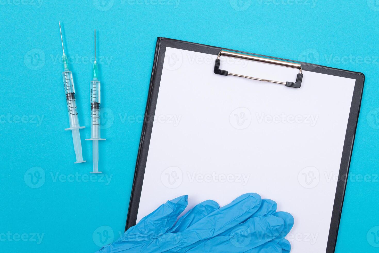 Vaccination, Immunology or Revaccination Concept - Two Medical Syringe Lying on Blue Table in Doctor's Office in a Hospital or Clinic. Black Clipboard with Sheet of Paper - Mock Up with Copy Space photo