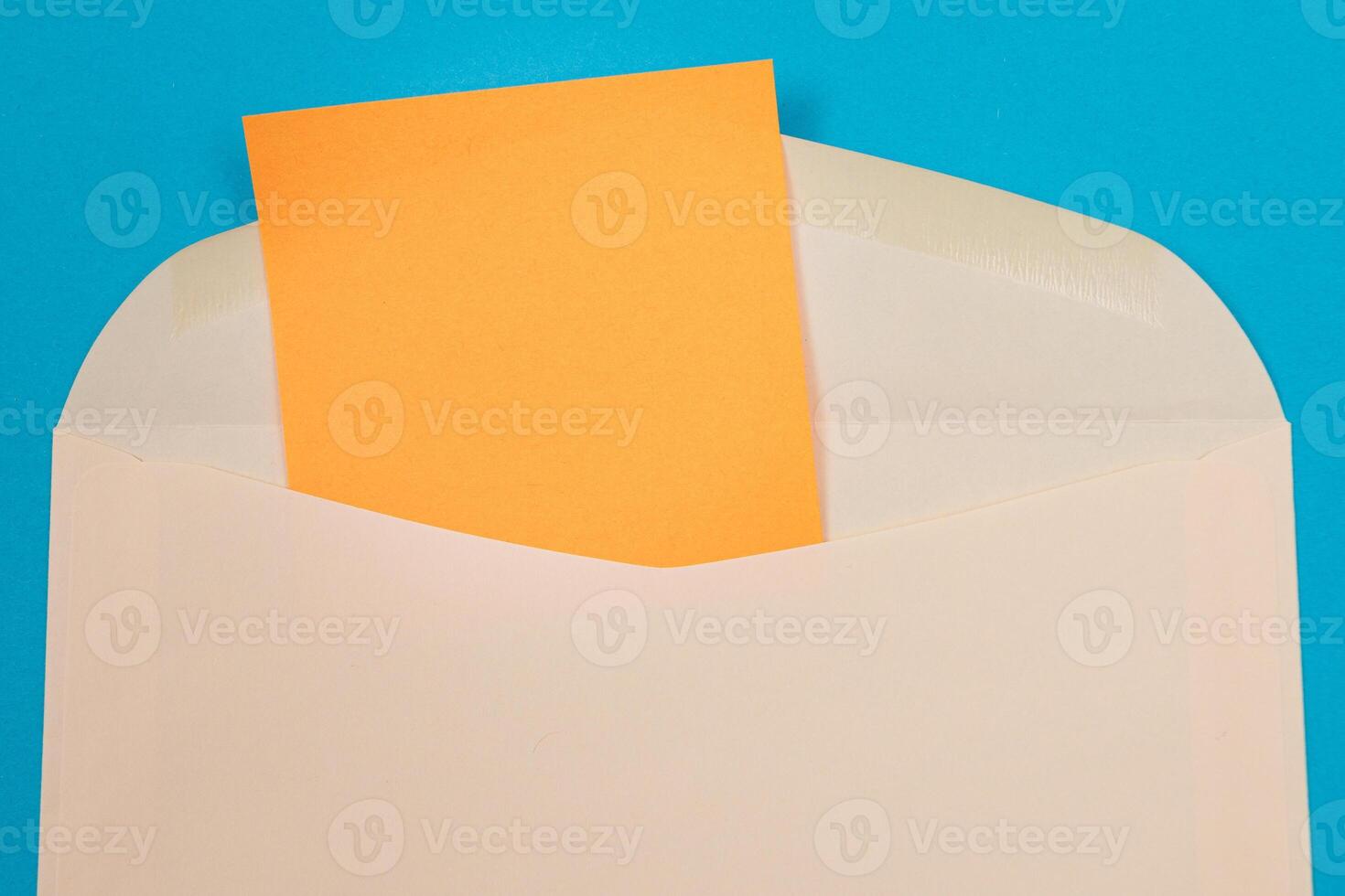 Beige Envelope with Blank Orange Sheet of Paper Inside, Lying on Blue Background - Mock Up with Copy Space. Receiving Mail or Notice, Sending Postcard - Top View, Flat Lay photo