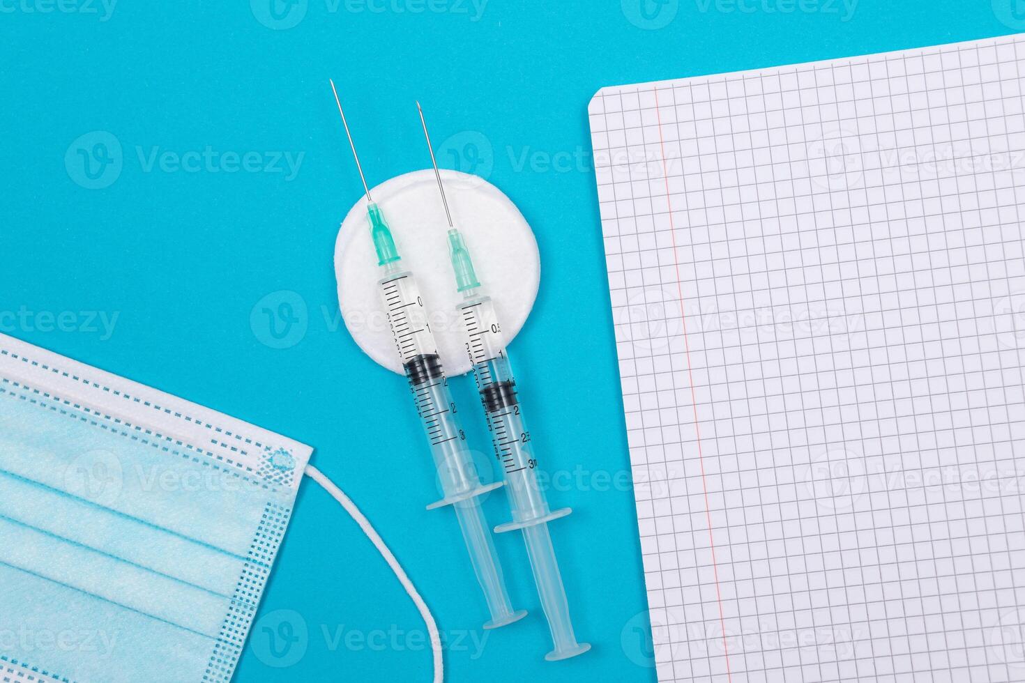 Vaccination, Immunology or Revaccination Concept - Two Medical Syringe Lying on Blue Table in Doctor's Office in a Hospital or Clinic. Opened Blank Notepad - Mock Up with Copy Space photo