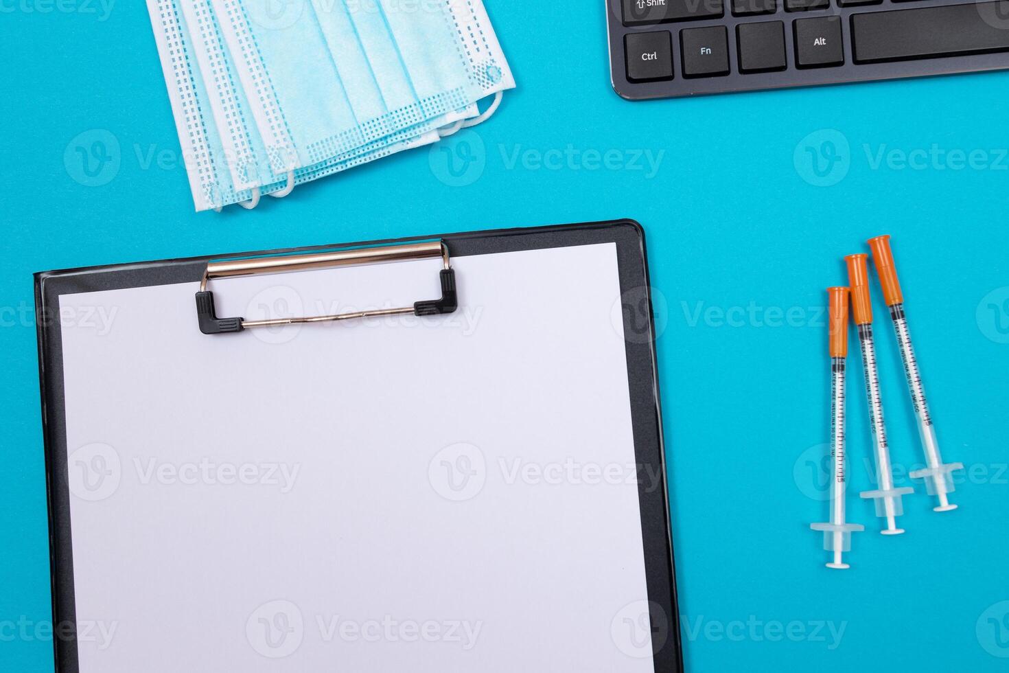 Vaccination, Immunology or Revaccination Concept - Three Insulin Syringe Lying on Blue Table in Doctor's Office in a Hospital or Clinic. Black Clipboard with Sheet of Paper - Mock Up with Copy Space photo