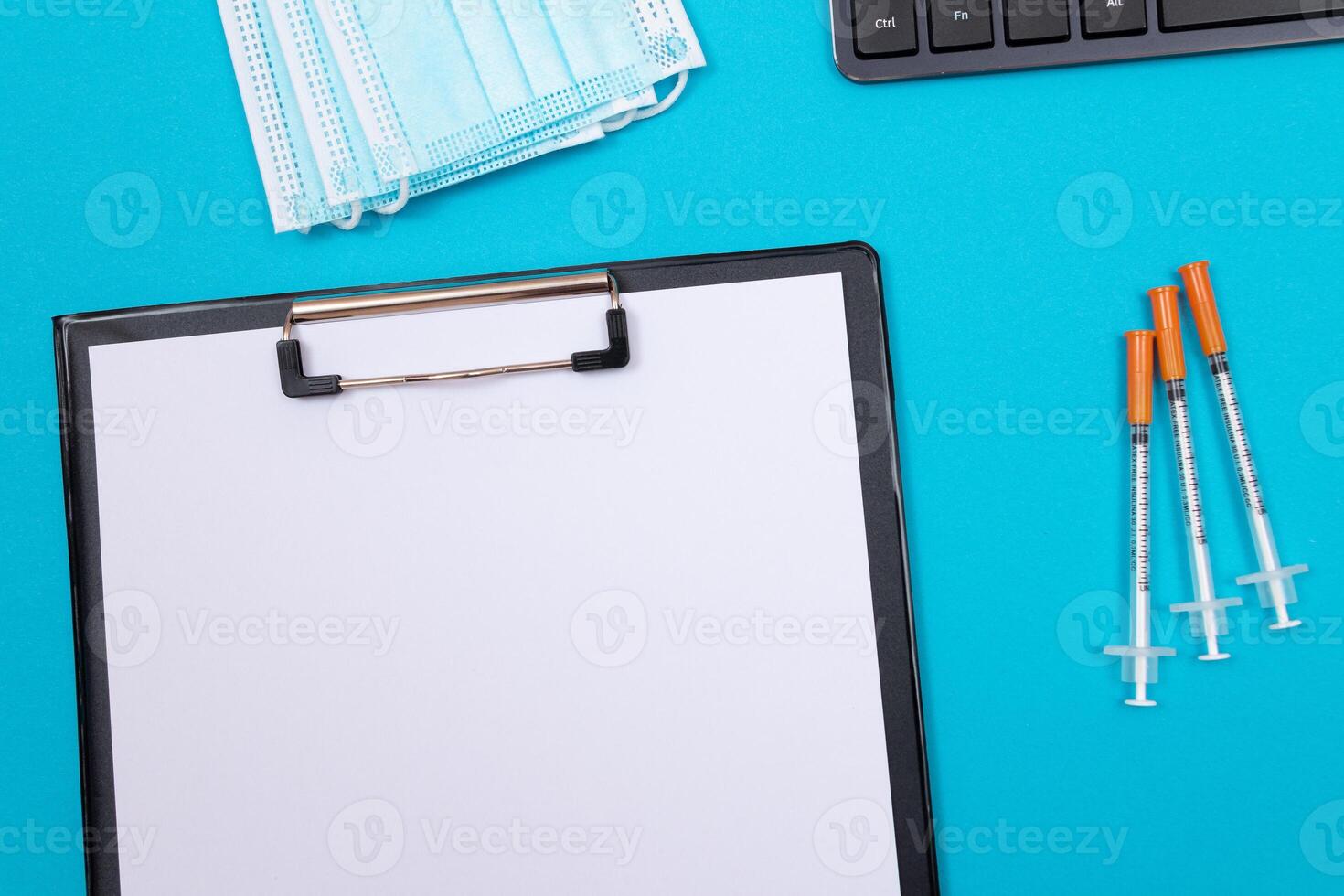 Vaccination, Immunology or Revaccination Concept - Three Insulin Syringe Lying on Blue Table in Doctor's Office in a Hospital or Clinic. Black Clipboard with Sheet of Paper - Mock Up with Copy Space photo