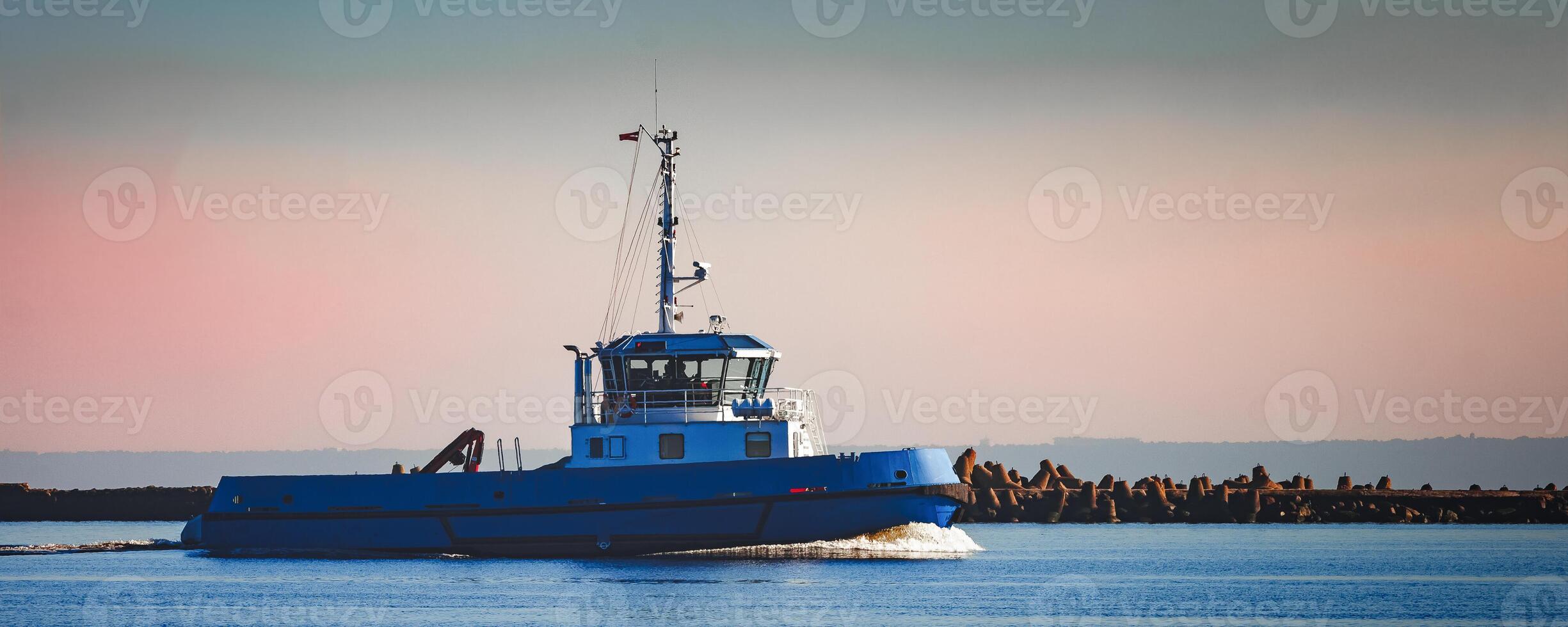 Blue small tug ship sailing past the breakwater dam in morning photo