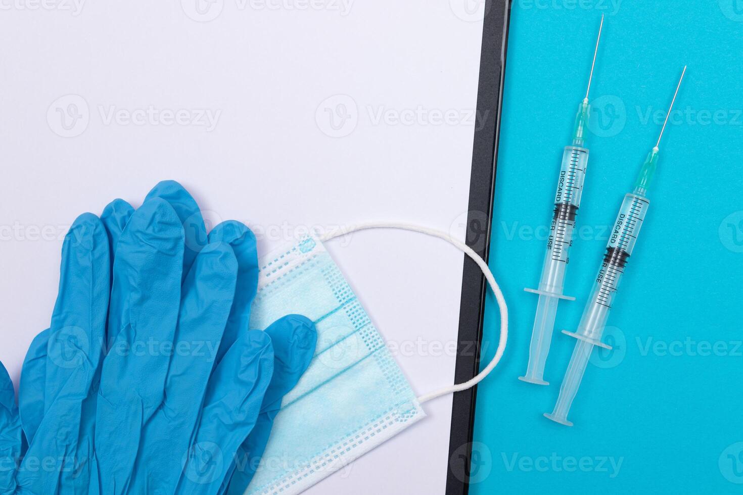 Vaccination, Immunology or Revaccination Concept - Two Medical Syringe Lying on Blue Table in Doctor's Office in a Hospital or Clinic. Black Clipboard with Sheet of Paper - Mock Up with Copy Space photo