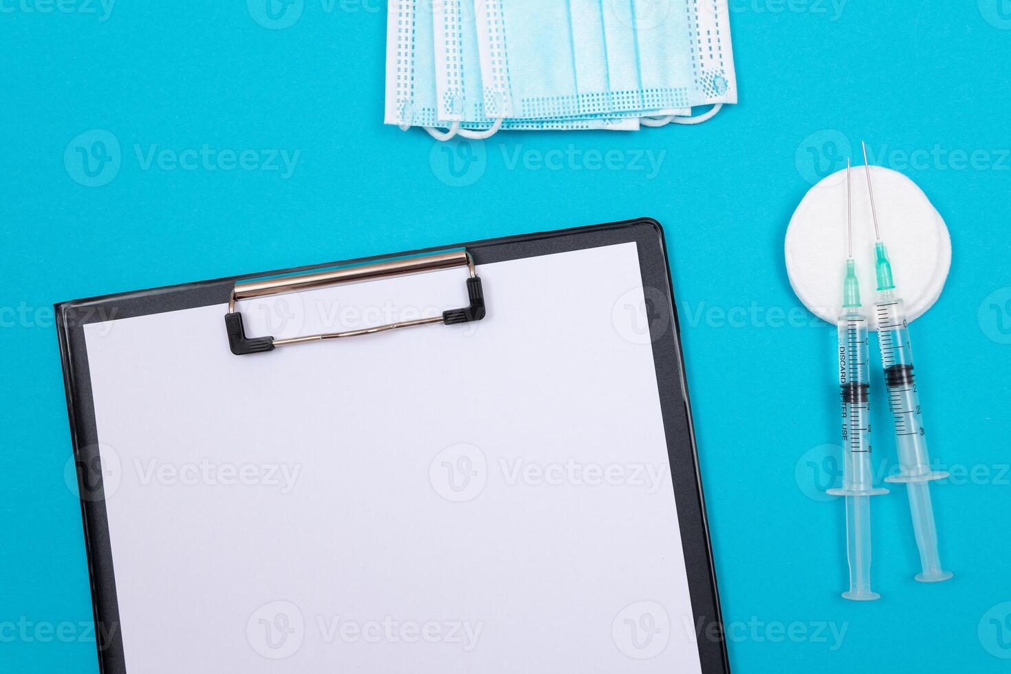 Vaccination, Immunology or Revaccination Concept - Two Medical Syringe Lying on Blue Table in Doctor's Office in a Hospital or Clinic. Black Clipboard with Sheet of Paper - Mock Up with Copy Space photo