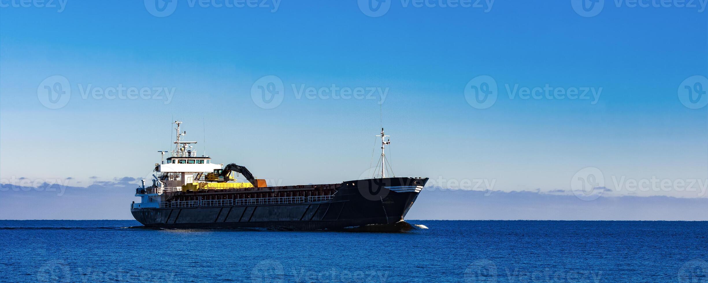 Black Sailing Bulk Carrier. Cargo Ship with Long Reach Excavator Moving in Still Water at Sunny Day by the Sea photo