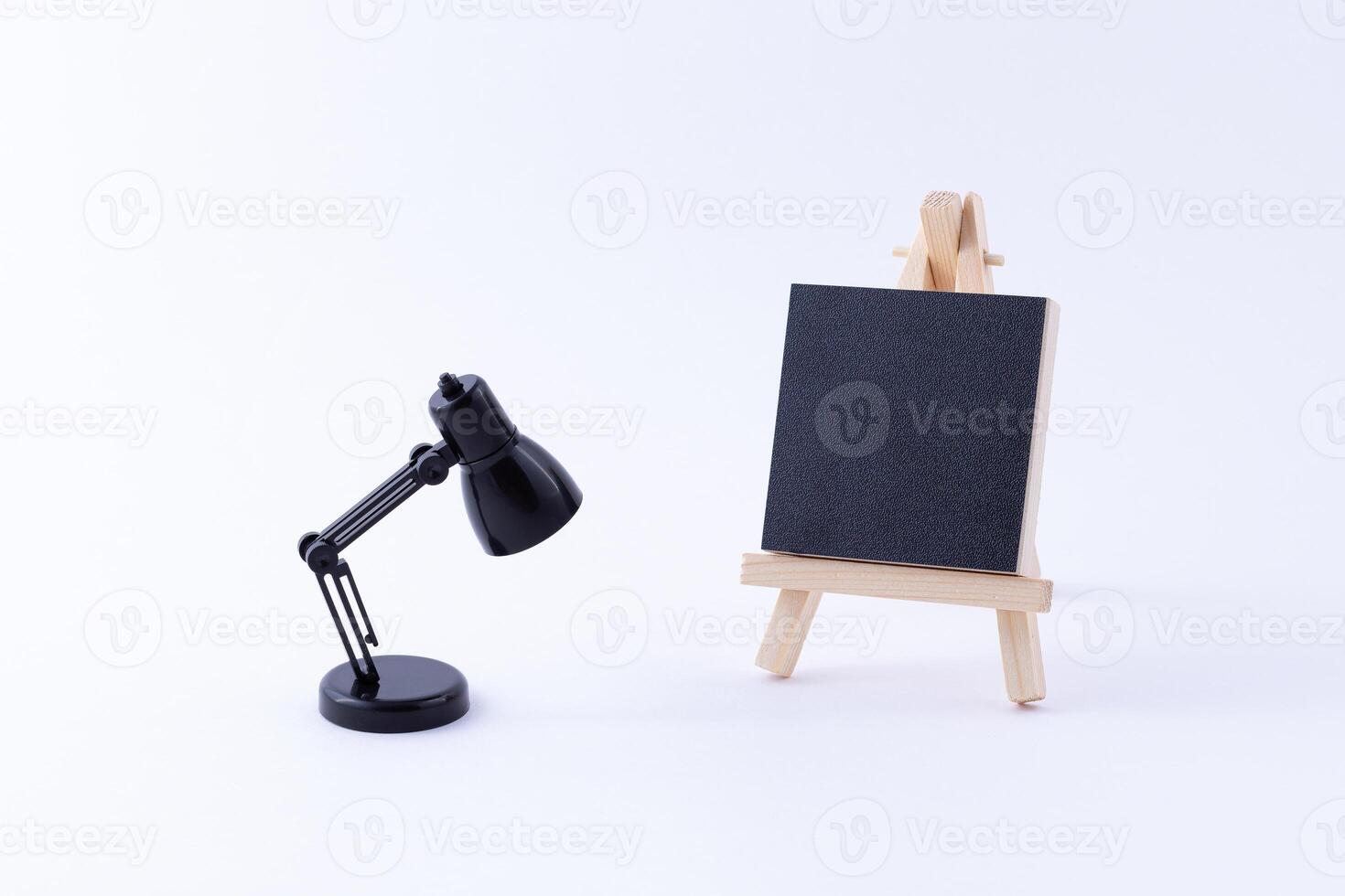 Wooden Easel Miniature with Blank Black Square Canvas for Artists and Painters - Mockup. Mini Wooden Stand with Clean Artboard and Small Black Table Lamp on White Background, Copy Space photo