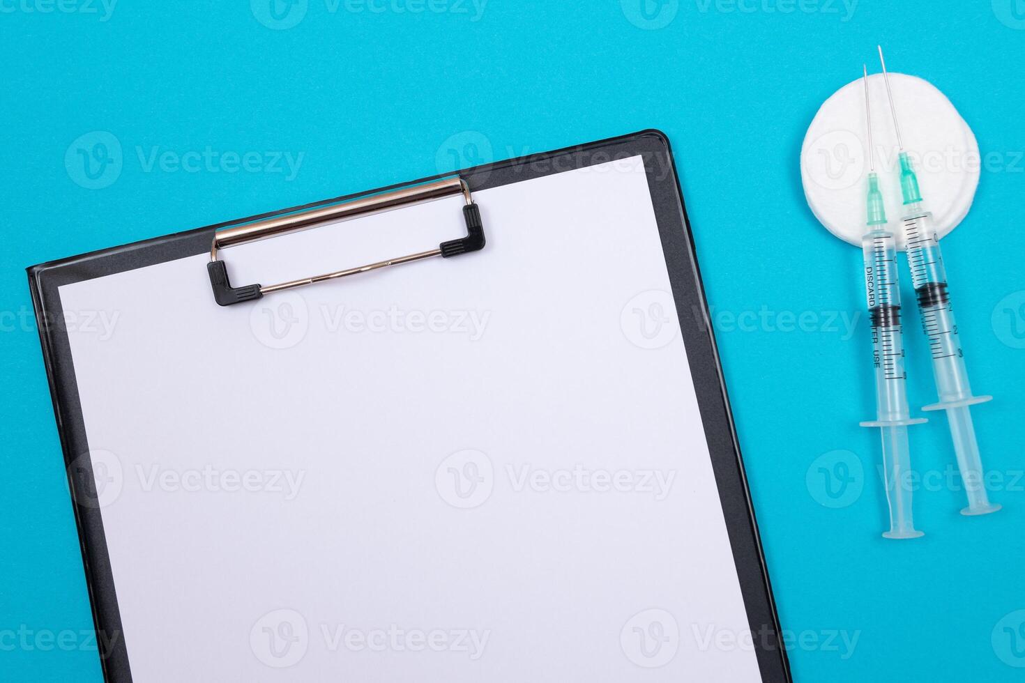 Vaccination, Immunology or Revaccination Concept - Two Medical Syringe Lying on Blue Table in Doctor's Office in a Hospital or Clinic. Black Clipboard with Sheet of Paper - Mock Up with Copy Space photo