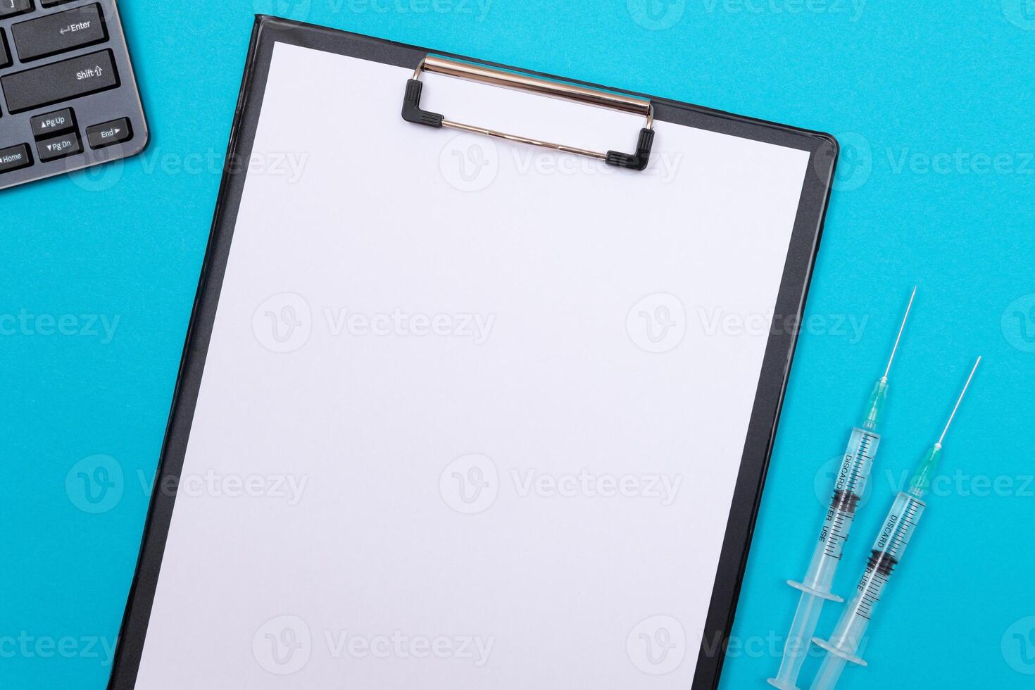 Vaccination, Immunology or Revaccination Concept - Two Medical Syringe Lying on Blue Table in Doctor's Office in a Hospital or Clinic. Black Clipboard with Sheet of Paper - Mock Up with Copy Space photo