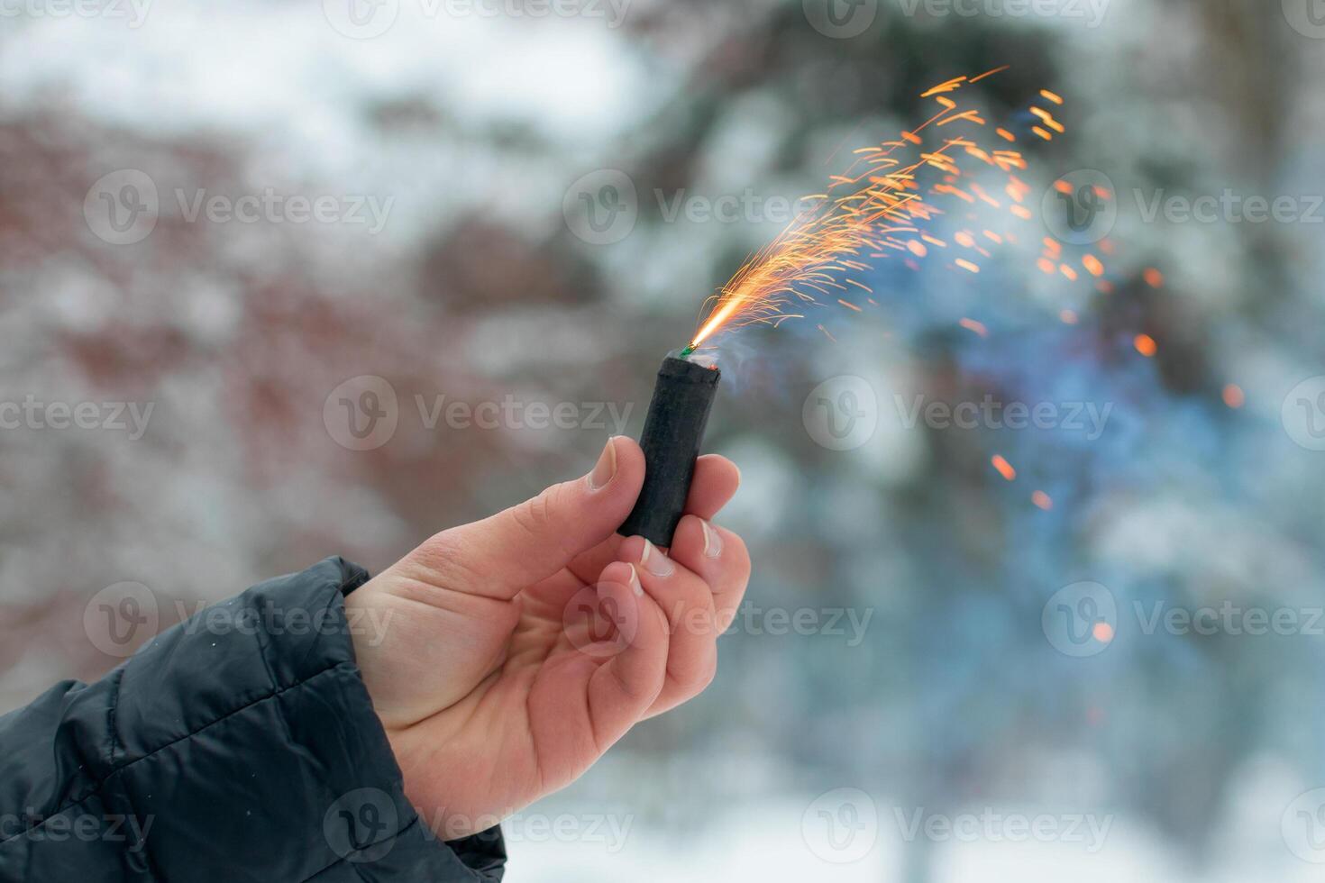 Burning Firecracker in a Hand. Guy Holding a Petard Outdoors in Winter at Daytime. Loud and Dangerous New Year's Entertainment. Hooliganism with Pyrotechnics. Noise of Firecrackers in Public Places photo