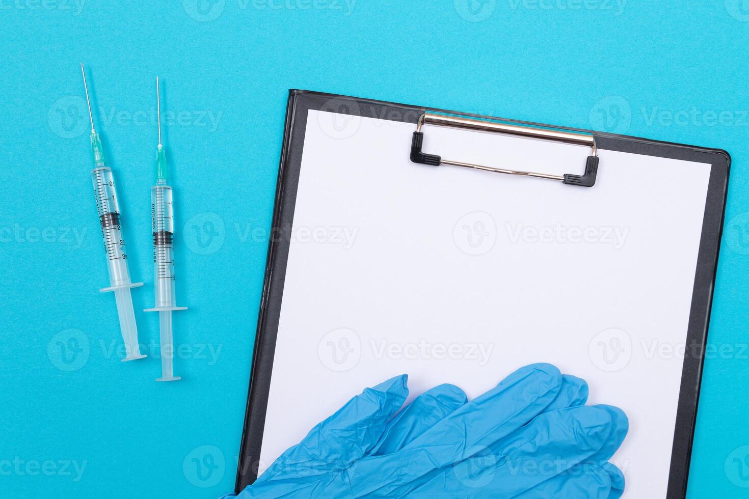 Vaccination, Immunology or Revaccination Concept - Two Medical Syringe Lying on Blue Table in Doctor's Office in a Hospital or Clinic. Black Clipboard with Sheet of Paper - Mock Up with Copy Space photo