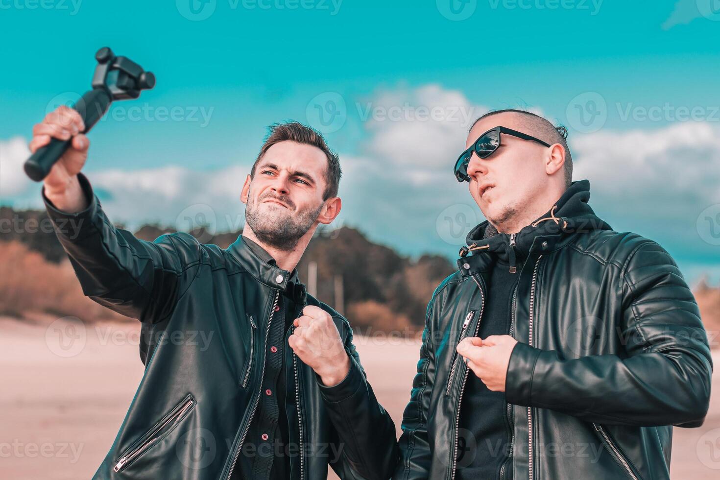 Two Handsome Male Friends Making Selfie Using Action Camera with Gimbal Stabilizer at the Beach. Youthful Men in Black Clothes Having Fun by Making Photos
